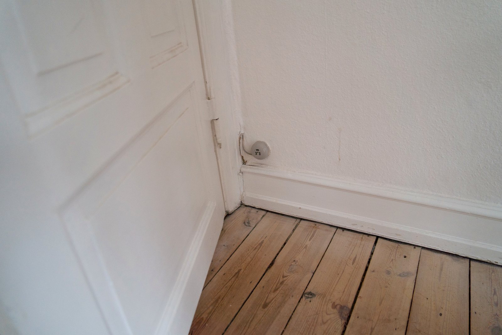 Detalje af slidt dør, fodpanel og gulv før istandsættelse
